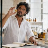 Parfumeur en laboratoire olfactif tenant un flacon de parfum de niche, comptoir avec flacons ambre et verre, lumière naturelle