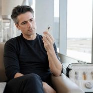 Homme en lounge d'aéroport examinant un atomiseur de parfum voyage, décantats et parfum solide visibles