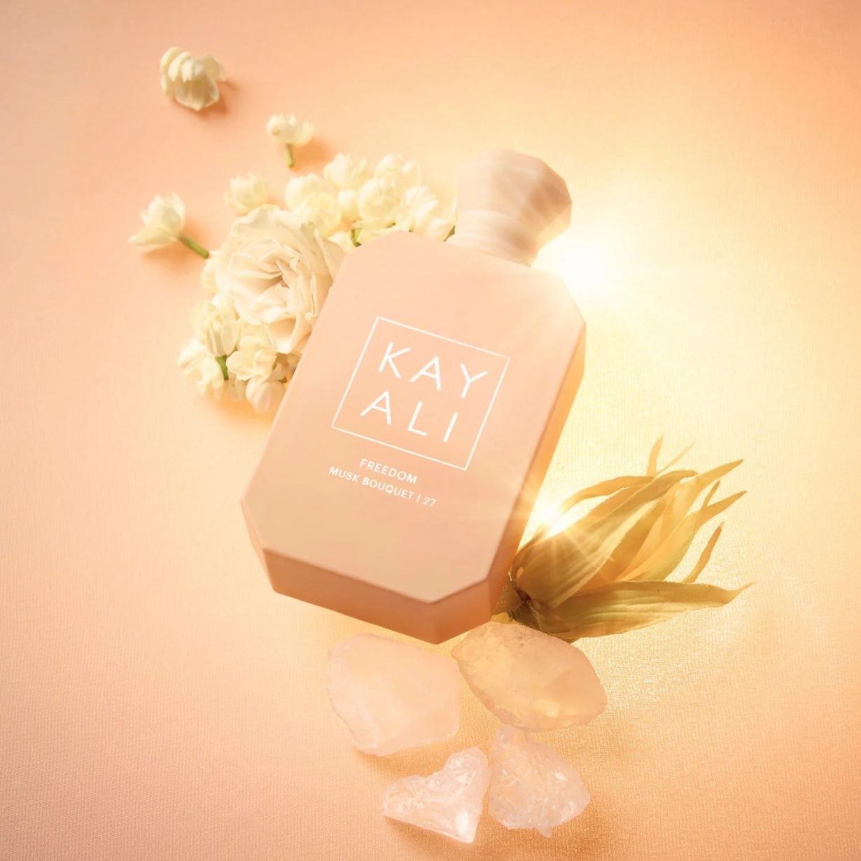 Flacon Kayali Freedom entouré de fleurs et cristaux