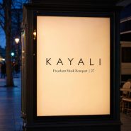 Affiche Kayali illuminée sur un boulevard au crépuscule